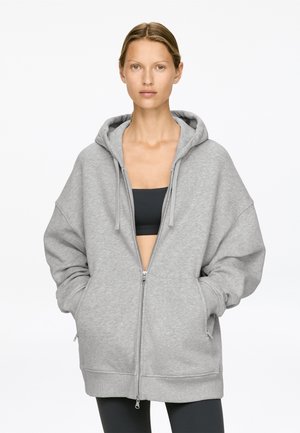 Hellgraue, oversized Zip-Hoodie aus weichem Stoff, mit großer Kapuze, Vordertaschen und gerippten Bündchen sowie Saum.