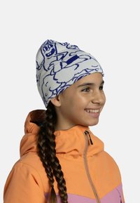 Knit beanie in white with blue cartoon design; soft texture, elastic fit. Worn by a child with long braided hair, paired with an orange jacket.