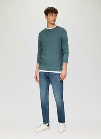 Pull en teal texturé avec des manches longues, col rond, associé à un jean bleu clair et des baskets blanches. Le pull a un petit détail de logo.