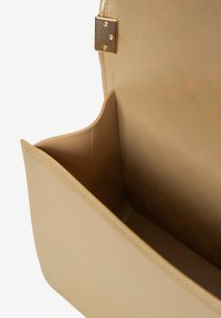 Interno di una borsa beige con una texture liscia, presenta una chiusura metallica con tre punti decorativi, ampio scomparto, lucentezza sottile.