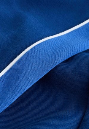 Tekstiilejä eri sinisen sävyissä, joissa on uurrettu rakenne ja valkoinen reunaviiva. Kangas vaikuttaa pehmeältä ja tiiviisti kudotulta.