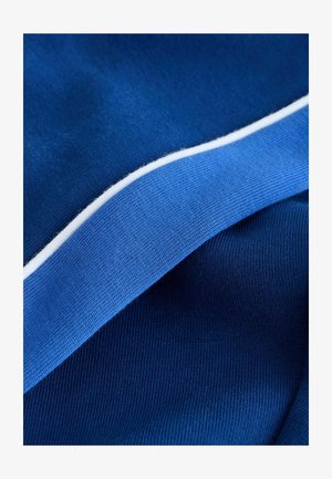 Tekstilės įvairių mėlynų atspalvių, su briaunotu paviršiumi ir baltu apvadu. Audinys atrodo minkštas ir tankiai austas.