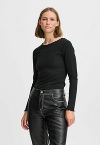 Crna rebrasta majica dugih rukava, uskog kroja. Uparena s crnim hlačama od umjetne kože koje imaju kontrastne bijele šavove i elegantan siluetu.