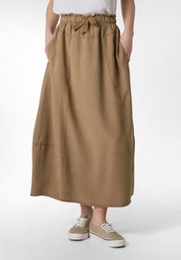 Falda larga marrón hecha de una tela suave, con una cintura elástica con un lazo, bolsillos laterales y detalles cosidos a lo largo de las costuras.