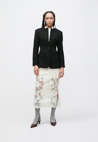 Fekete, texturált blézer egygombos záródással, fehér virágos csipkerokival rétegezve. Szürke térdzokni és bordó magassarkú cipő egészíti ki a megjelenést.