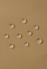 Klare, runde Wassertropfen sind auf einem strukturierten, beigen Stoffhintergrund verteilt, was die wasserabweisenden Eigenschaften des Materials unterstreicht.