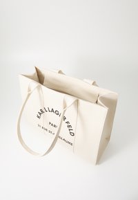 Canvas tote väska i krämfärg, med dubbla handtag, tryckt text som lyder "KARL LAGERFELD" och "21 RUE ST-GUILLAUME," samt med dragkedjeslut.