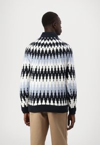 Maglione lavorato a maglia in blu, bianco e nero, con un motivo geometrico a zig zag, colletto alto e polsini e orlo a costine.