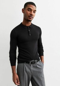 Zwarte polo met lange mouwen, een kraag en knoopsluiting. Getailleerd ontwerp met geribbelde manchetten, gecombineerd met geruite broeken en een zwarte riem.
