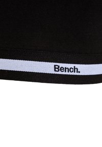 Črn material z širokim elastičnim pasom z belim trakcem in natisnjenim logotipom "Bench." Gladka tekstura, oprijet dizajn.
