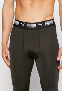 Leggings sportivi neri caratterizzati da un design aderente, una trama liscia e un'ampia cintura elastica con il marchio "PUMA BASKETBALL".