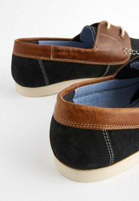 Scarpe nere in suede con un accento in pelle marrone, caratterizzate da una finitura testurizzata, cuciture a contrasto e una suola in gomma bianca.