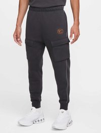 Mörkgrå Nike-joggingbyxor med elastisk midja, sidofickor och detaljer i orange; har en avsmalnande benpassform och kontrasterande vit kant.