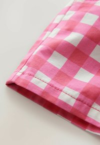 Tissu vichy rose et blanc avec une texture lisse, présentant un motif à carreaux. Le bord présente une couture soignée.