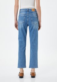 Ljust blå, högmidjade jeans med avslappnad passform, med bakfickor och en läderpatch på midjan, visade från baksidan.