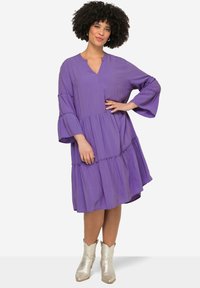 Violetti virtaava mekko V-kaula-aukolla, kolmen neljänneksen kellohihat, kerrostettu muotoilu ja joustavat yksityiskohdat. Yhdistetty hopeisiin cowboy-saappaisiin.