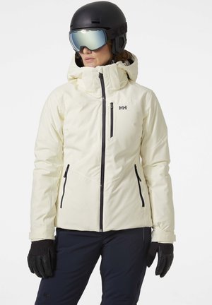 Witte skijack met een capuchon, voorzien van zwarte ritsen en zakken. Gecombineerd met zwarte handschoenen en een zwarte helm met goggles.