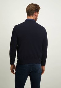 Dunkelblauer Strickpullover mit langen Ärmeln, gerippten Bündchen und Saum sowie einem klassischen Kragen. Getragen mit dunklen Jeans, die ein schlichtes Design zeigen.