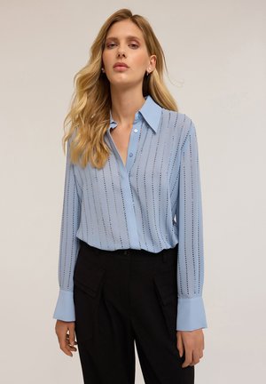 Lichtblauw overhemd met verticale strepen en zilveren studs, met lange mouwen en een klassieke kraag, gecombineerd met zwarte broeken.