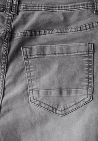 Tela de mezclilla gris con un bolsillo trasero central; el bolsillo tiene una forma triangular, una línea de costura a lo largo de los bordes y una textura suave.