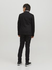 Svart kavaj med en kroppsnära design, tillsammans med matchande byxor. Avslappnade svarta sneakers fulländar outfiten. Slät tygkvalitet, inga synliga mönster.