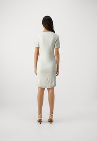 Šviesiai pilka, iki kelių ilgio suknelė iš mezgimo audinio, su raštuotomis sidabrinėmis trumpomis rankovėmis, apvaliu iškirpimu ir prigludusia siluetu, derinama su atvirais aukštakulniais.