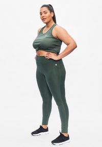 Groene sportieve crop top met knoopontwerp, gecombineerd met bijpassende high-waisted leggings. Beide items hebben een gladde textuur en een aansluitende pasvorm.