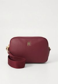 Bordeauxrote Umhängetasche aus glattem synthetischem Material, mit einem goldenen Logo und einem gewebten Riemen. Rechteckige Form mit abgerundeten Kanten.