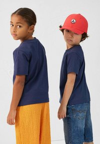 T-shirts en coton navy portés par deux enfants ; l'un en pantalon orange texturé, l'autre en short en jean et portant une casquette rouge avec un logo.
