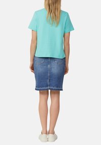 Un haut turquoise à manches courtes est associé à une jupe crayon en denim bleu avec un ourlet effiloché, portée avec des baskets blanches.