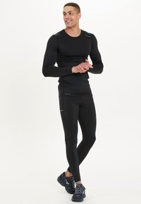 Zwarte langetermijnsportshirt met lange mouwen en aansluitende leggings, gemaakt van rekbare stof met een gladde textuur en reflecterende accenten, gecombineerd met donkere sneakers.