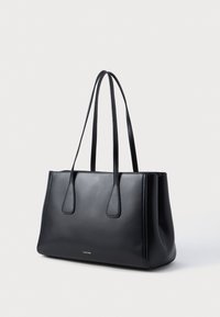 Μαύρη δερμάτινη τσάντα tote με λείο φινίρισμα, επιμηκημένες διπλές λαβές, ορθογώνιο σχήμα και διακριτική λογότυπη λεπτομέρεια μπροστά.
