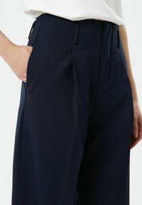 Pantalon bleu marine à coupe décontractée, doté de poches latérales et d'une texture de tissu lisse, confectionné avec un pli net à l'avant.