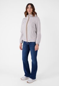 Giacca a vento grigio chiaro con cappuccio, dotata di cerniera frontale e accento a strisce colorate. Abbinata a jeans svasati blu scuro e scarpe bianche.