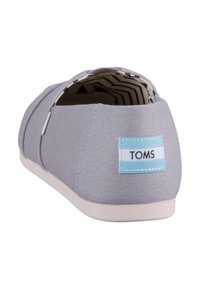 Scarpa slip-on in tela grigia con suola in gomma bianca. Presenta un'etichetta TOMS blu sul retro e una fodera interna a righe.