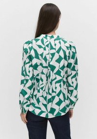Grön och vit mönstrad blus med lång ärm, texturerad tyg, rundad halsringning och knapppartidig detalj på baksidan. Bärs med mörka jeans.