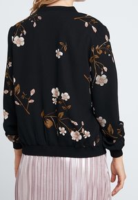 Giacca bomber nera con ricami floreali in rosa e marrone. Polsini e orlo a coste, tessuto liscio e vestibilità comoda.