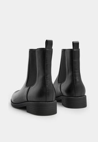 Mustat nahkaiset Chelsea-saappaat, joissa on elastiset sivupaneelit, vetonauha ja massiivinen kumipohja. Silkkinen pinta ja tyylikäs muotoilu.