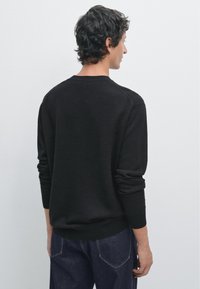 Czarny sweter dzianinowy z długimi rękawami i ściągaczami, z okrągłym dekoltem i luźnym fasonem. Noszony z ciemnymi dżinsami.