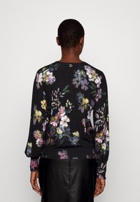 Schwarzer Pullover mit floralem Muster, langen Ärmeln, gerippten Bündchen und einem kleinen Logodetail am Nacken. Weicher, strukturierter Stoff.