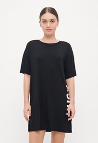 Juoda per didelė t-shirt su trumpomis rankovėmis, apvaliu kaklu ir balta grafika šone. Minkšta, lygi medžiaga, laisvas fasonas.