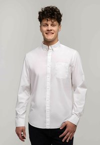 Biała koszula z długim rękawem, wykonana z gładkiej bawełny. Posiada wywinięty kołnierzyk, długie rękawy oraz jedną kieszeń na piersi po lewej stronie.