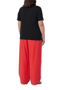 Zwarte korte mouwen t-shirt gecombineerd met losse, lichte, felrode wijde broeken. Glad materiaal met minimale details.