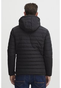 Polstret svart jakke med hette, med quiltet tekstur og stripete ermer, båret med blå denimjeans.