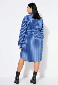 Robe chemise rayée bleue avec une taille ceinturée, des manches longues, des poignets à bouton et une coupe décontractée, associée à des bottines noires à talons carrés.