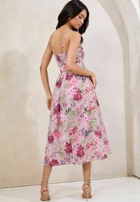 Abito maxi floreale in rosa con schiena arricciata, spalline sottili regolabili e una silhouette fluida; presenta una combinazione di motivi floreali in rosa e verde.