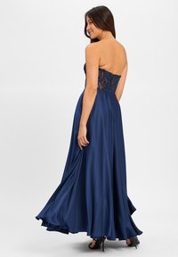 Robe de soirée longue bleu marine avec un corsage sans bretelles orné de perles et une jupe en satin fluide, présentant une texture lisse et une légère traîne.