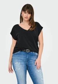 T-shirt noir à manches courtes en V associé à un jean en denim bleu déchiré et une ceinture noire avec des accents circulaires en argent.