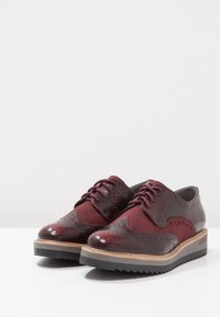 Burgundské kožené boty s brogue detaily, semišovými akcenty a stohovanou podrážkou s vroubkovaným vzorem. K odlučení designu přispívají tkaničky a zaoblená špička.