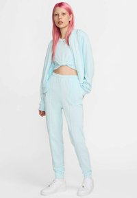 Tuta azzurro chiaro in tessuto morbido, composta da un top corto, felpa con cappuccio e zip integrale, e pantaloni aderenti con polsini elastici. Scarpe da ginnastica bianche.